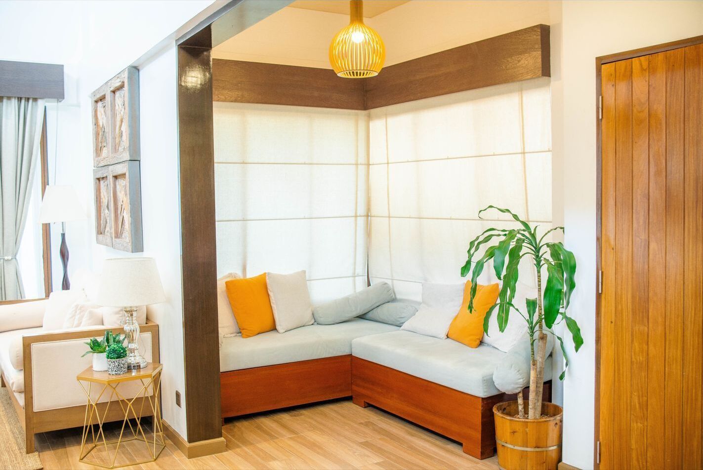 Una sala de estar en esquina con un sofá modular, piso de madera, una planta en maceta y una puerta de madera.