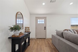 Un salon moderne avec un canapé gris, une console noire agrémentée d’un miroir et un plancher en bois.