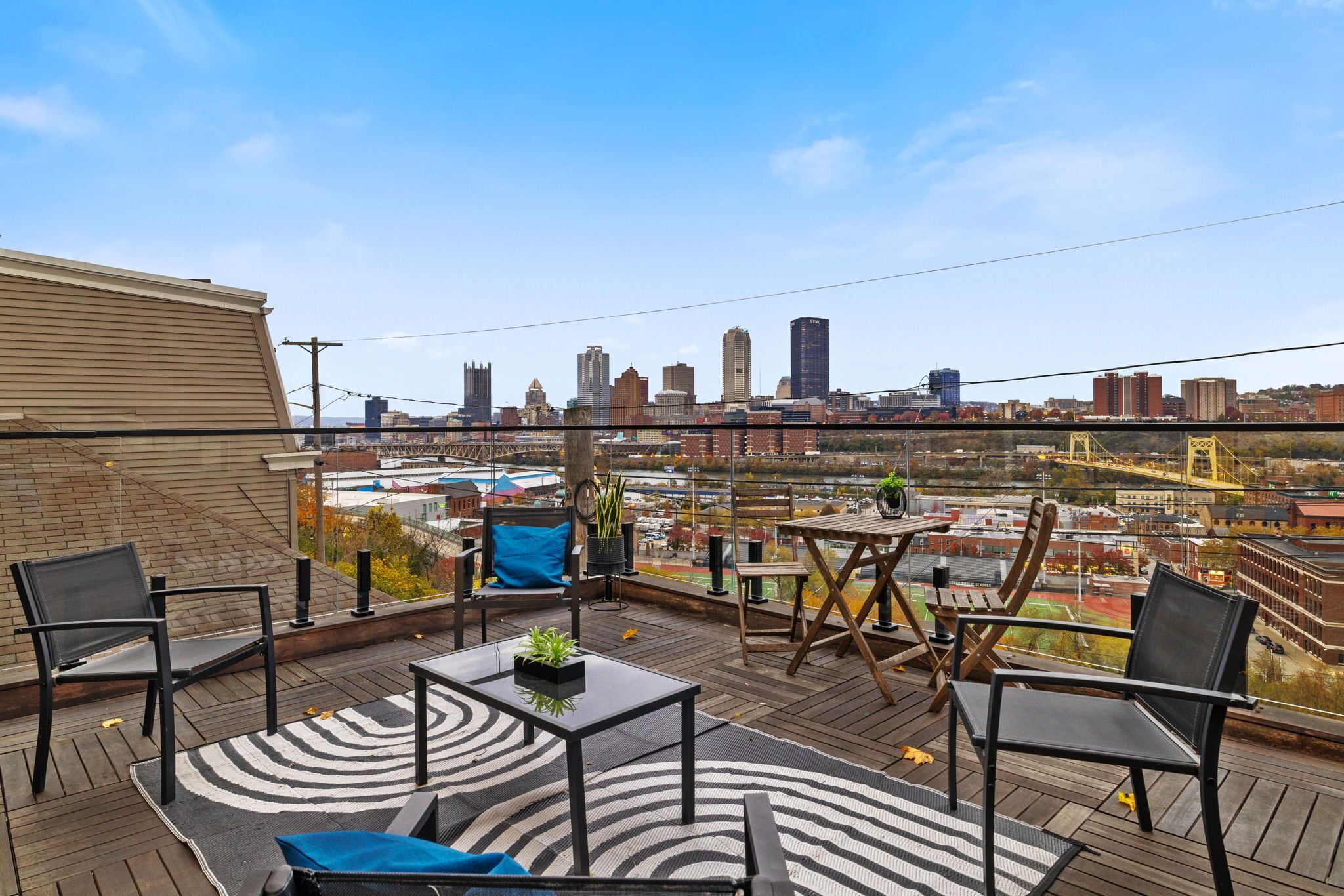 A rooftop patio with a city view, featuring a table, chairs, and a patterned rug.