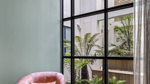Een kamer met een groot raam, een roze stoel en uitzicht op groen buiten.