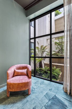 A room with a large window, a pink chair, and a view of greenery outside.