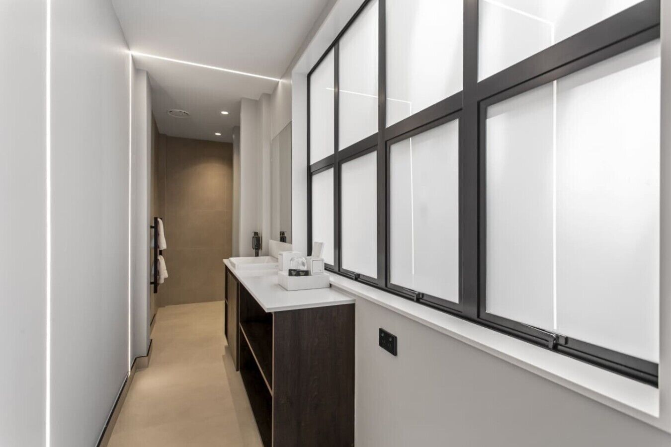 A modern bathroom with a large window, a white sink, and a dark wooden cabinet.