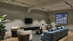 Een moderne woonkamer met een bank, fauteuils, een salontafel en een aan de muur bevestigde televisie.
