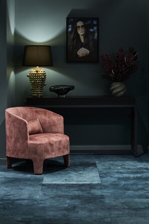 A room with a pink armchair, a dark console table, a lamp, a framed picture, and a vase with flowers. - The Sanctuary Suite — Quiet, Dark & Deeply Restful (Auckland)