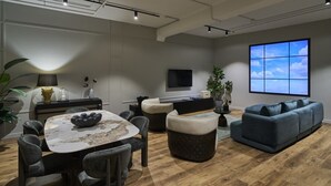 Un soggiorno moderno con un tavolo rotondo, divani scuri e un grande schermo televisivo.