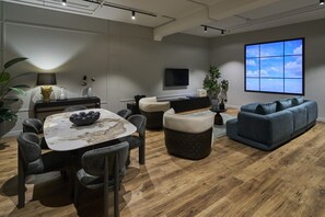 A modern living room with a round table, dark sofas, and a large TV screen. - The Sanctuary Suite — Quiet, Dark & Deeply Restful (Auckland)