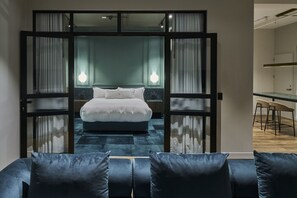 A modern bedroom with a large bed, a desk, and a chair in a separate area. - The Sanctuary Suite — Quiet, Dark & Deeply Restful (Auckland)