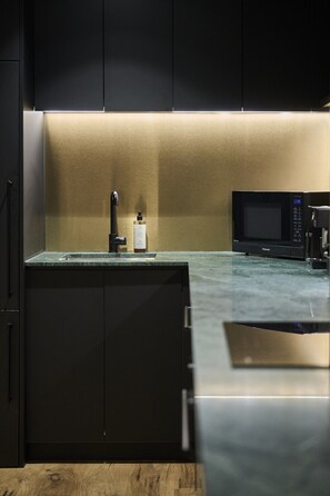 A modern kitchen with a built-in microwave, a faucet, and a bottle on the counter. - The Sanctuary Suite — Quiet, Dark & Deeply Restful (Auckland)