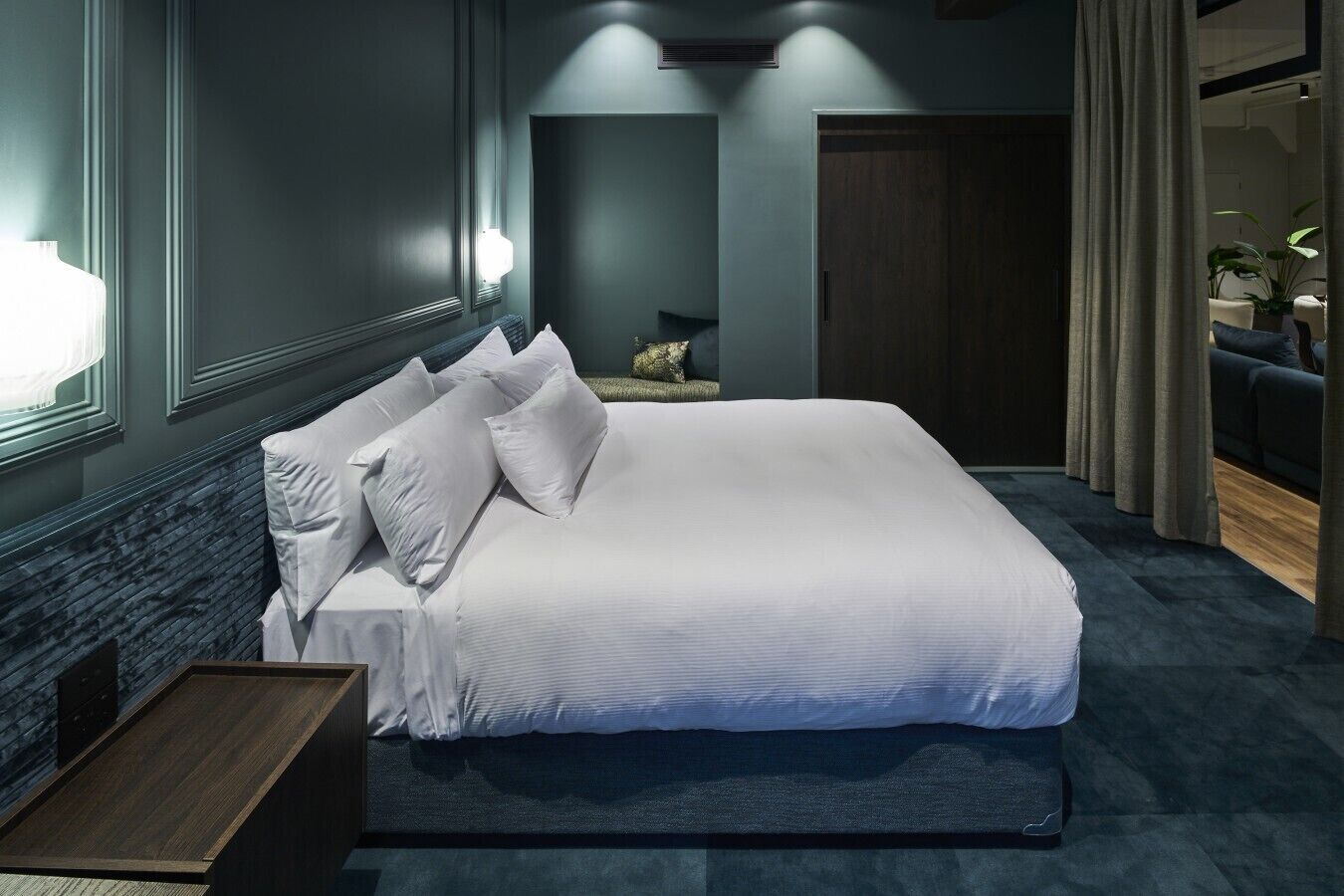 Une chambre d’hôtel moderne avec un grand lit, une table de chevet, une moquette sombre et une vue sur l’extérieur.