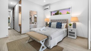 Ein modernes Schlafzimmer mit einem Bett, Nachttischen, einer Bank und Blick ins Freie.