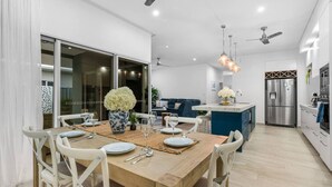 Eine moderne Küche mit einer zentralen Kochinsel, einem Essbereich mit einem Holztisch und weißen Stühlen sowie einem großen Fenster, das natürliches Licht hereinlässt.