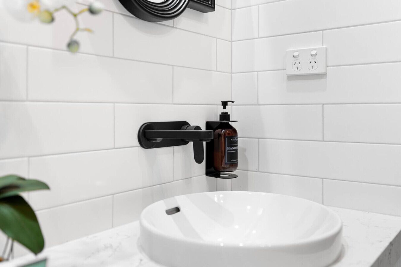 Ein Badezimmer mit einem weißen Waschbecken, einem schwarzen Seifenspender und einer weißen Fliesenwand.