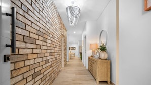 Ein Korridor mit Backsteinwand, Holzboden, einem Holzkabinett und einem hängenden Kronleuchter.