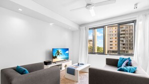 A modern living room with a flat-screen TV, grey sofas, a coffee table, and a large window with a city view.