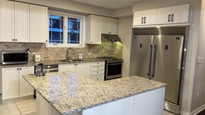 A modern kitchen with white cabinets, a granite countertop, stainless steel appliances, and a window with a view of the outside.