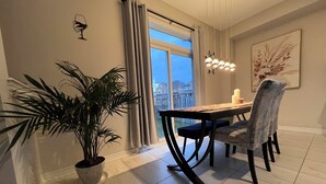 A dining area with a table, chairs, a potted plant, a window with curtains, and a hanging light fixture.