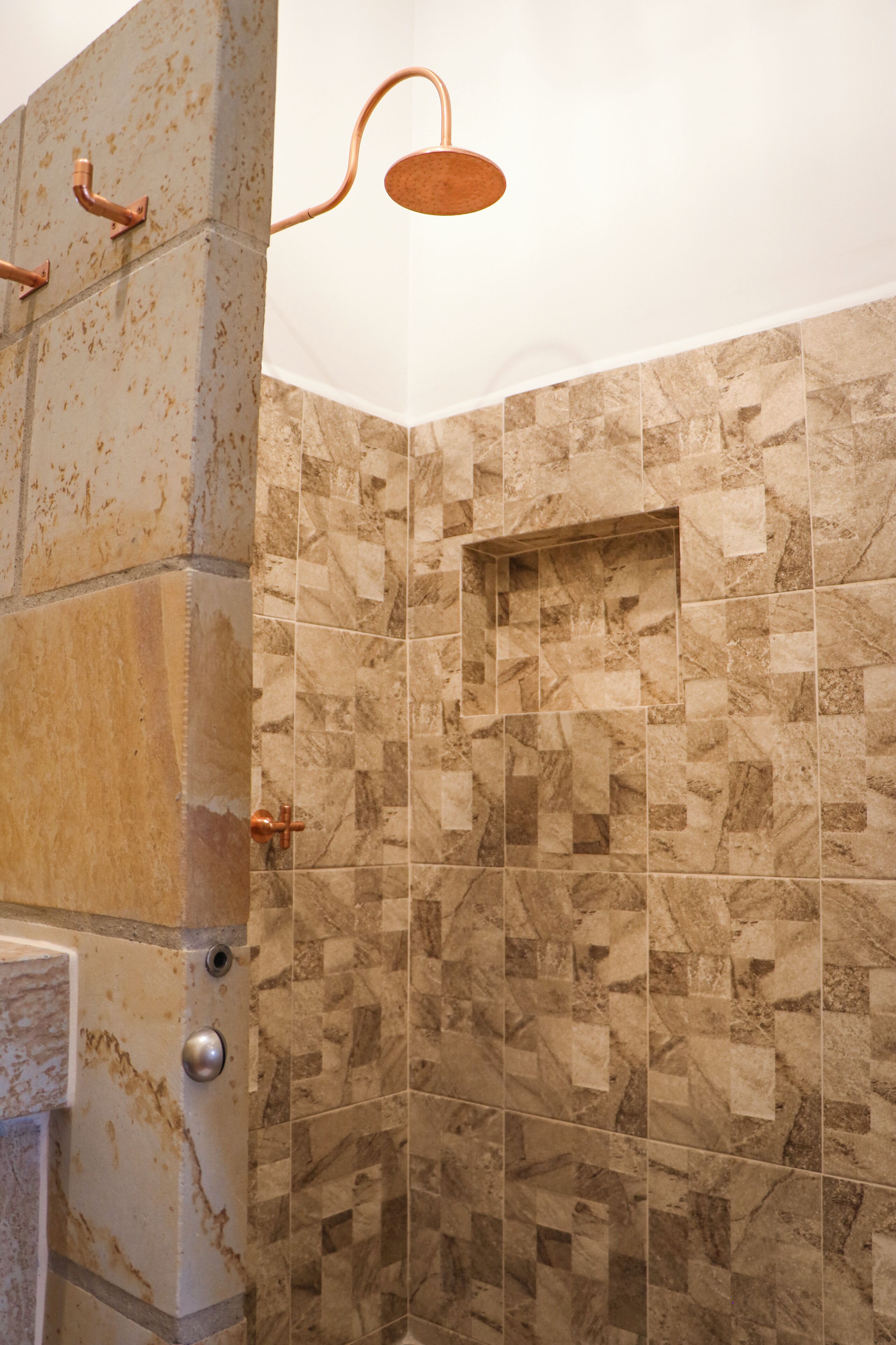 A shower with a copper fixture and a tiled wall with a geometric pattern.