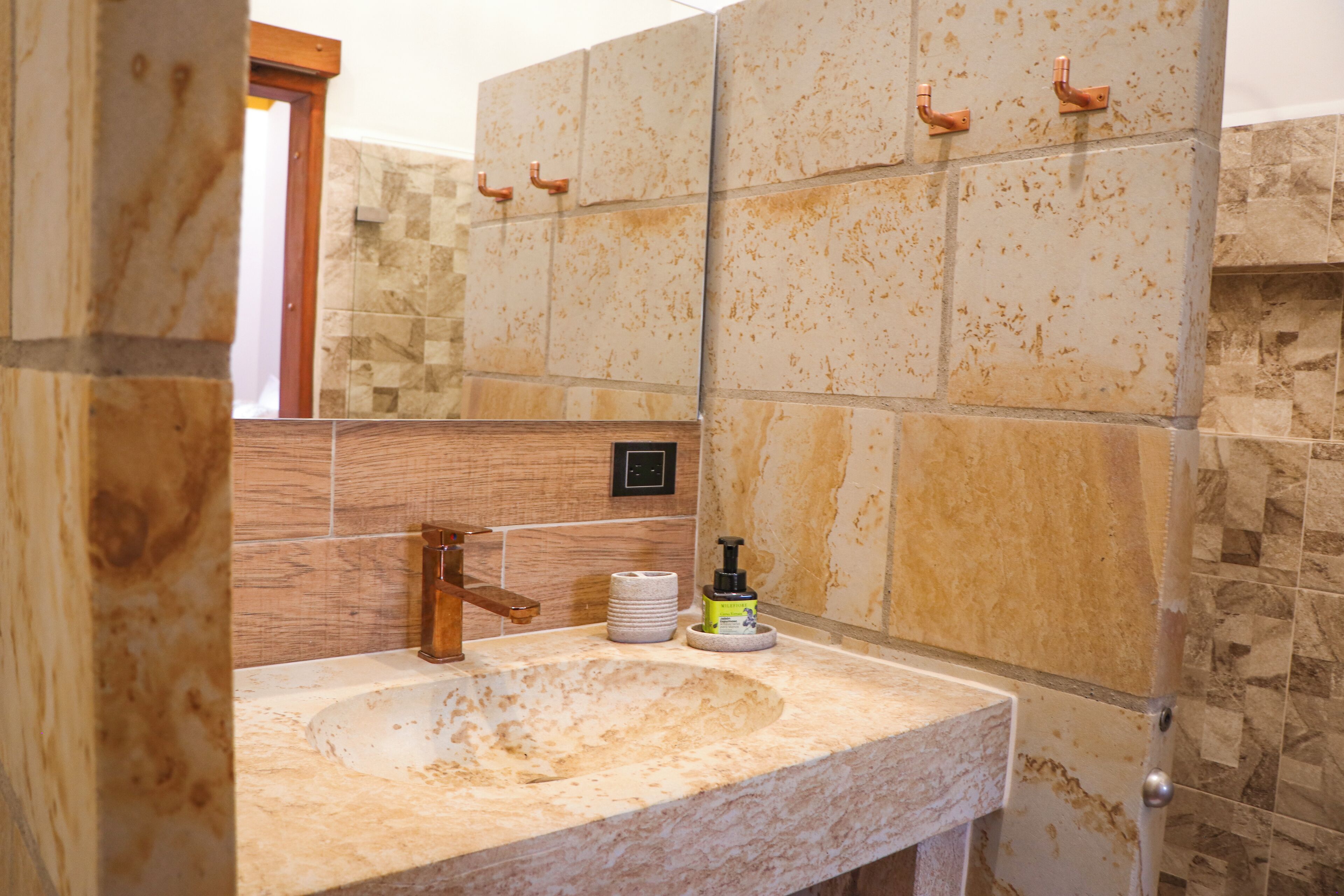 A bathroom with a marble sink, wooden vanity, and stone tiles.