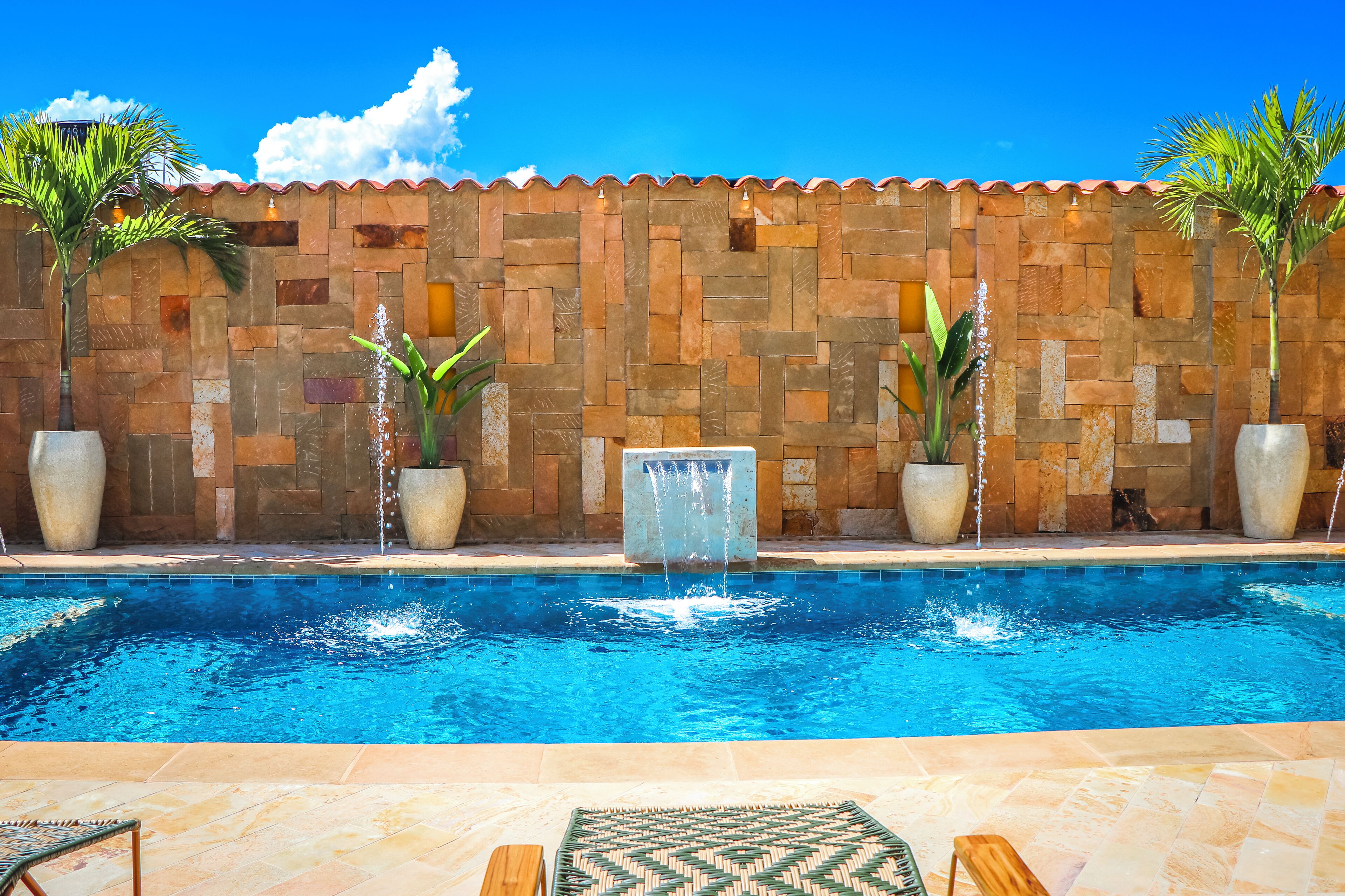 Una piscina con muro de piedra, fuentes de agua y plantas en macetas.
