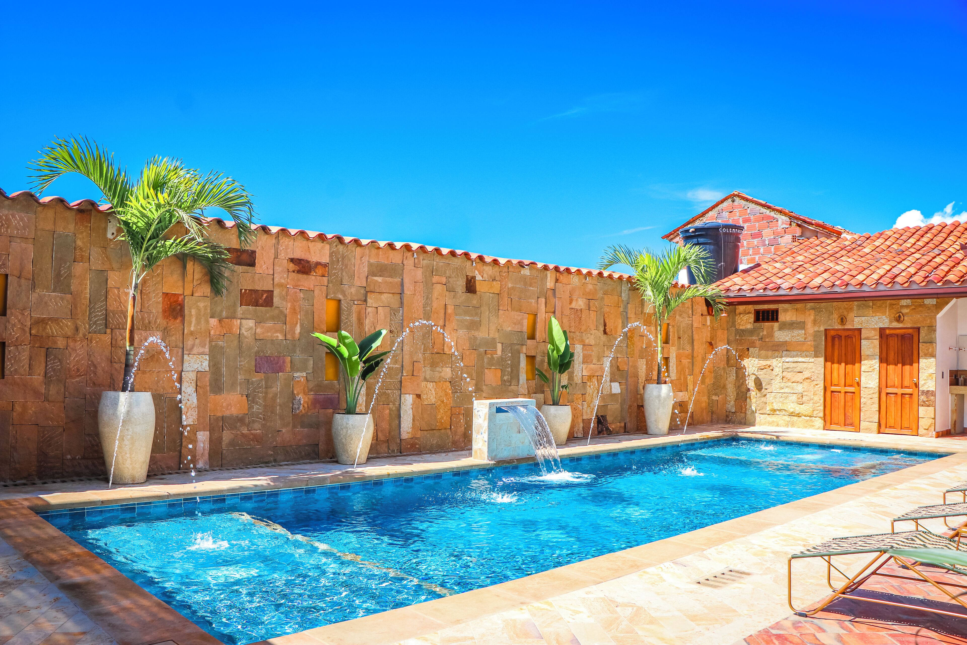 Piscina con fuentes y elementos acuáticos, rodeada de muros de piedra y plantas en macetas.