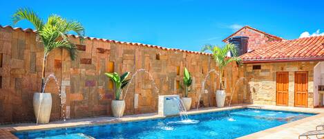 Piscina con fuentes y elementos acuáticos, rodeada de muros de piedra y plantas en macetas.
