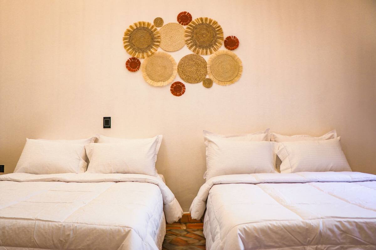 A hotel room with two beds, a wall-mounted decorative item, and a small electrical outlet.