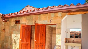 A stone building with a tiled roof, a wooden door, and a bathroom with a sink and mirror. - Hotel Boutique Casa Trilo (Barichara)