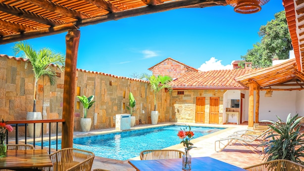 A poolside area with stone walls, wooden furniture, and a clear blue pool. - Hotel Boutique Casa Trilo (Barichara)