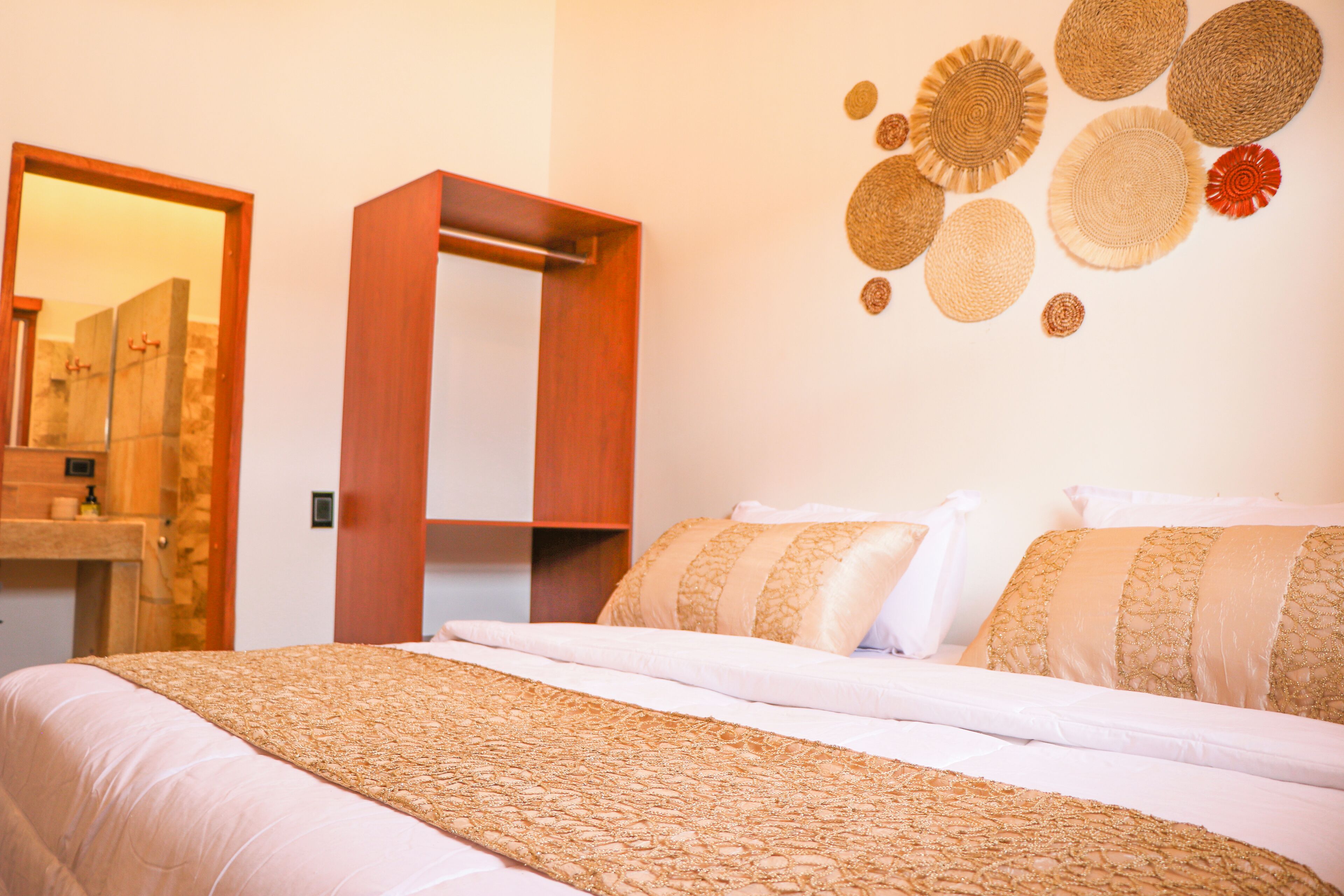 Een net opgemaakt bed met een bedsprei met patroon, een houten kledingkast en een wand met geweven wanddecoratie.