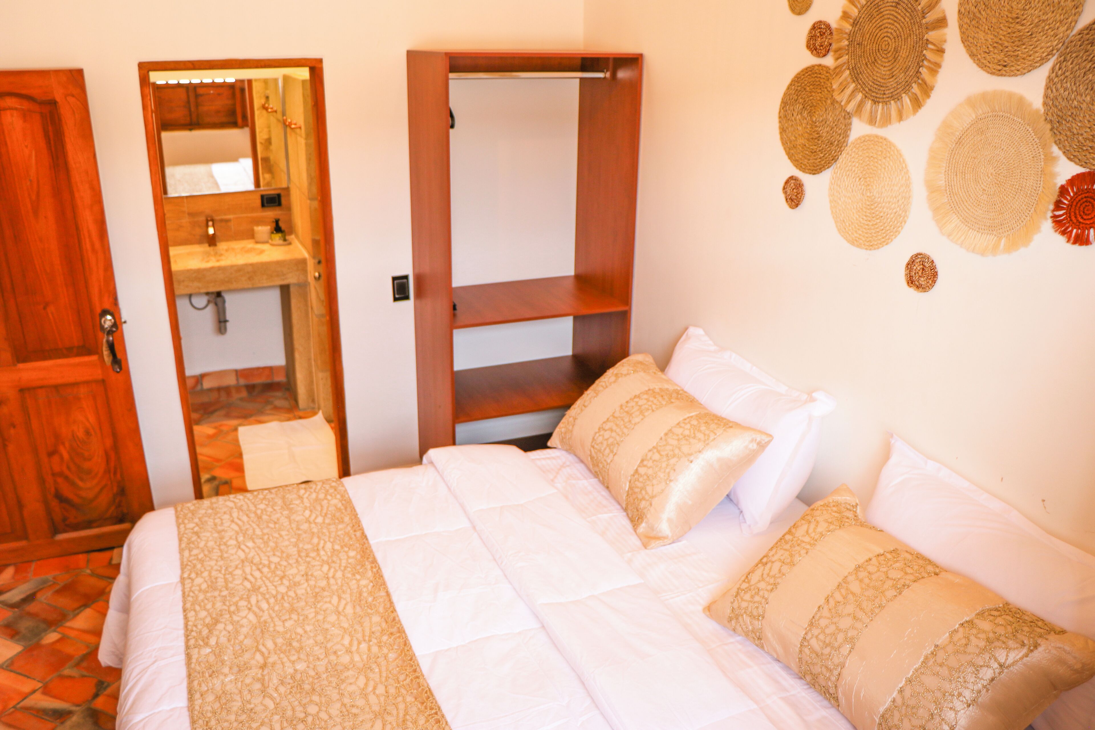 A bedroom with a bed, a wooden wardrobe, a bathroom with a mirror, and a wall with decorative items.