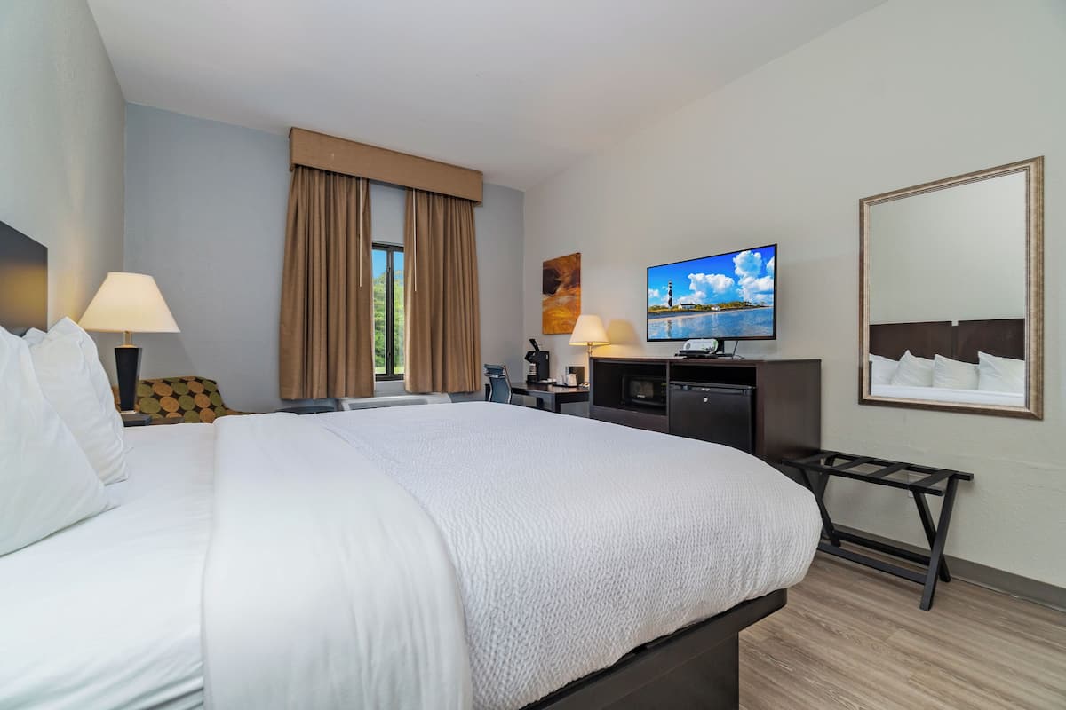 Une chambre d’hôtel avec un grand lit, un bureau avec un ordinateur, une télévision et une fenêtre avec des rideaux.