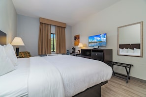 Habitación de hotel con una cama grande, un escritorio con computadora, televisor y ventana con cortinas.