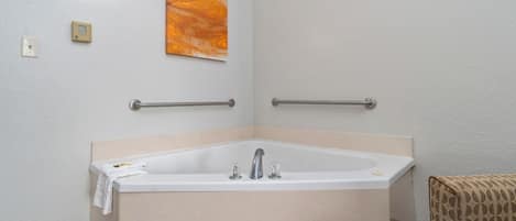 Ein Badezimmer mit Badewanne, Haltegriffen, einem Handtuch, einer Wandleuchte und einem Gemälde.