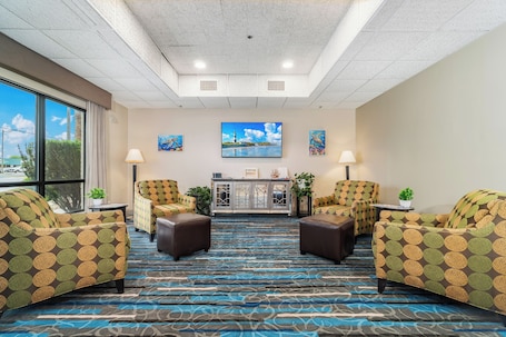 A hotel lobby with patterned armchairs, a large flat-screen TV, and a view of the outdoors through large windows.. The Windstar Hotel - Emerald Isle / Swansboro