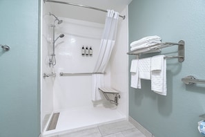 Ducha a pie con puerta de vidrio, regadera, ducha de mano, toallero con toallas y escurridor para artículos de baño.