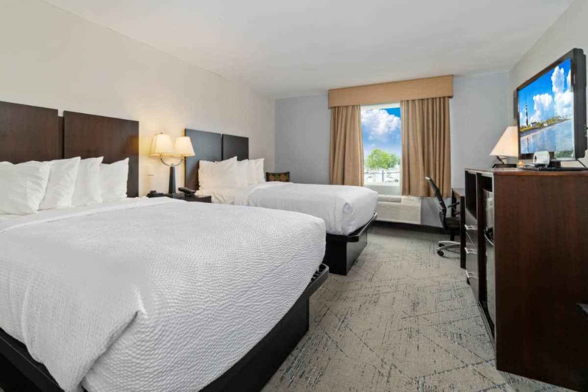 Une chambre d’hôtel avec deux lits, une télévision, un bureau et une fenêtre avec des rideaux.