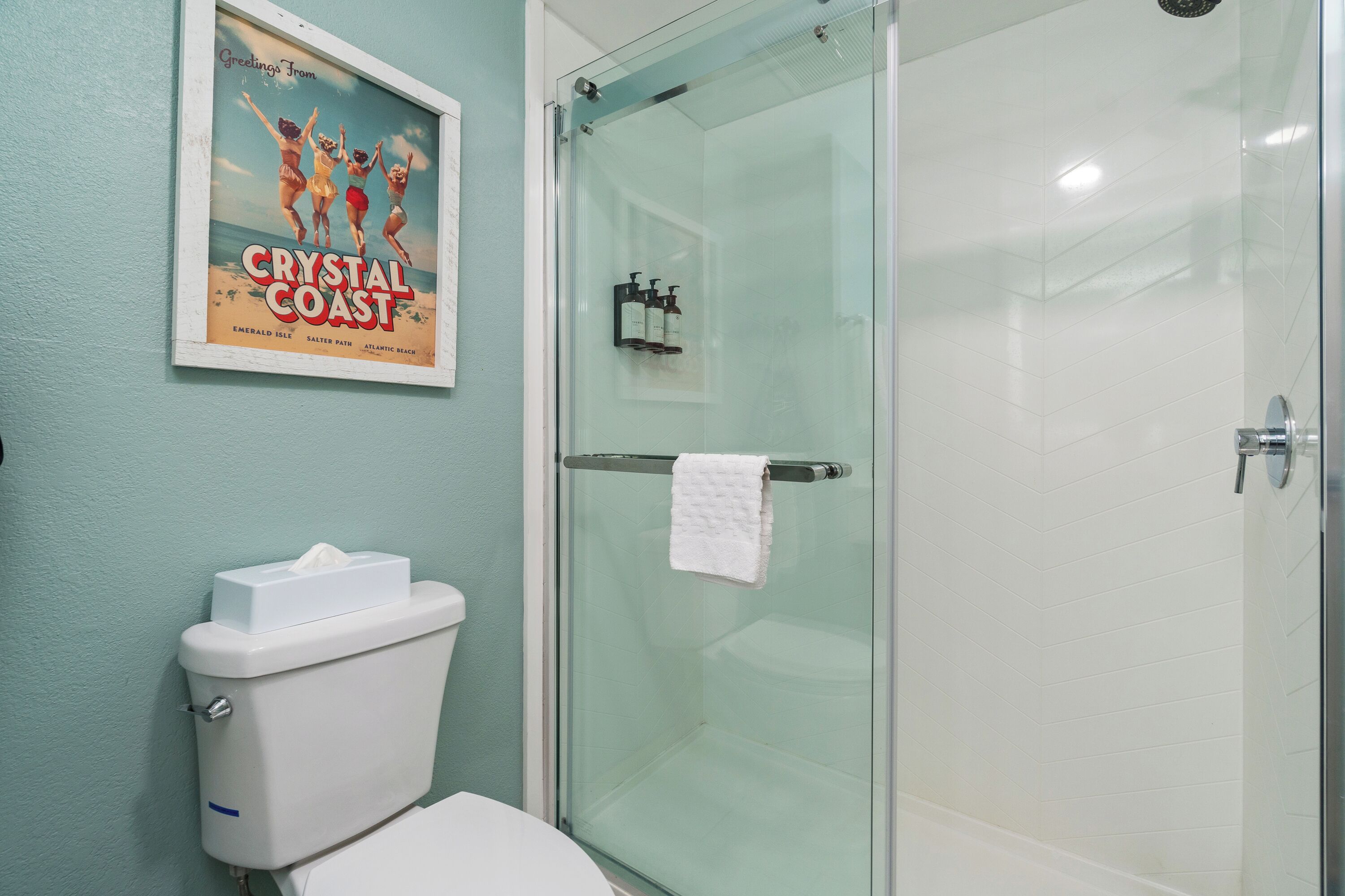 A bathroom with a glass shower enclosure, a toilet, and a poster on the wall.