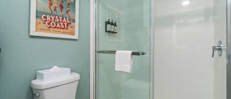 A bathroom with a glass shower enclosure, a toilet, and a poster on the wall.