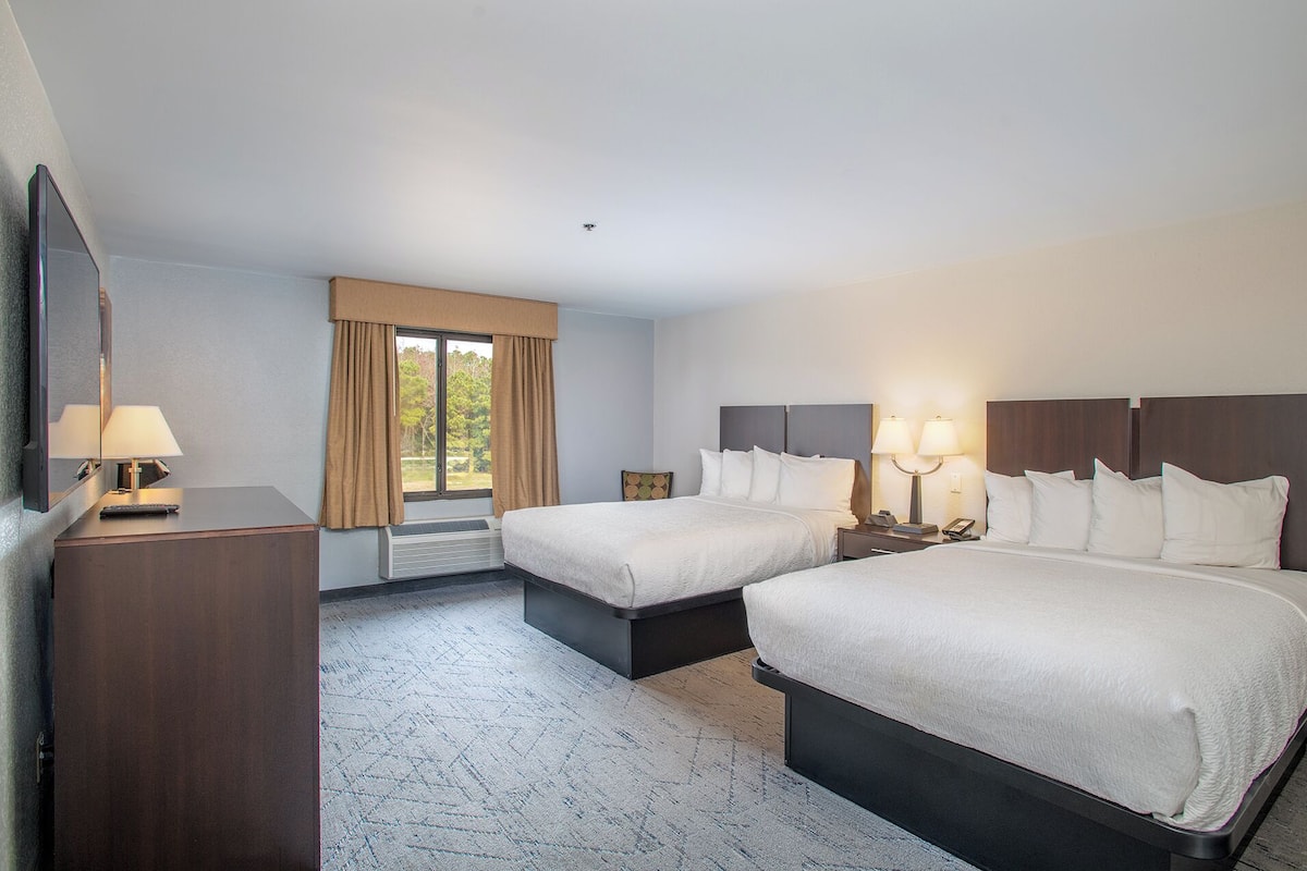 Une chambre d’hôtel avec deux lits, un bureau, une chaise, une fenêtre avec des rideaux et un téléviseur fixé au mur.