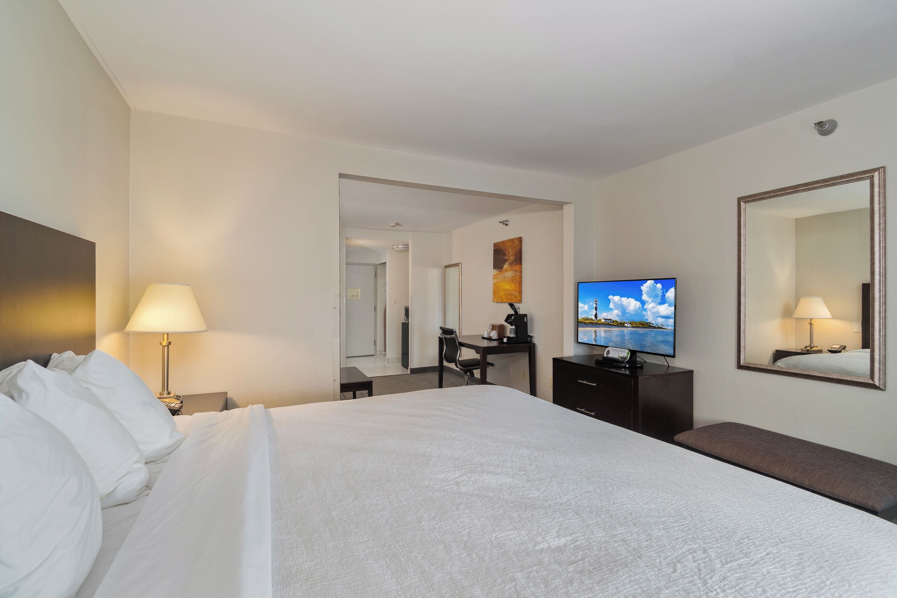 A hotel room with a large bed, a desk with a computer, a television, and a mirror.