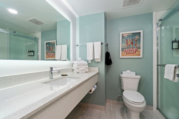 A bathroom with a glass shower enclosure, a white sink with a mirror, and a toilet. - The Windstar Hotel - Emerald Isle / Swansboro (Cedar Point)
