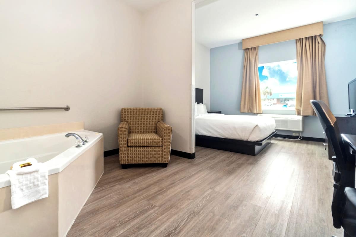 Une chambre d’hôtel avec une baignoire, une chaise, un lit et un bureau.