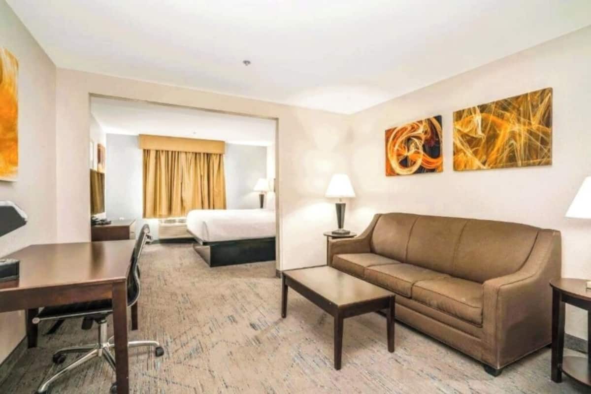 Une chambre d’hôtel avec un lit, un canapé, un bureau et une chaise. Il y a deux lampes sur le canapé et une lampe sur le bureau.