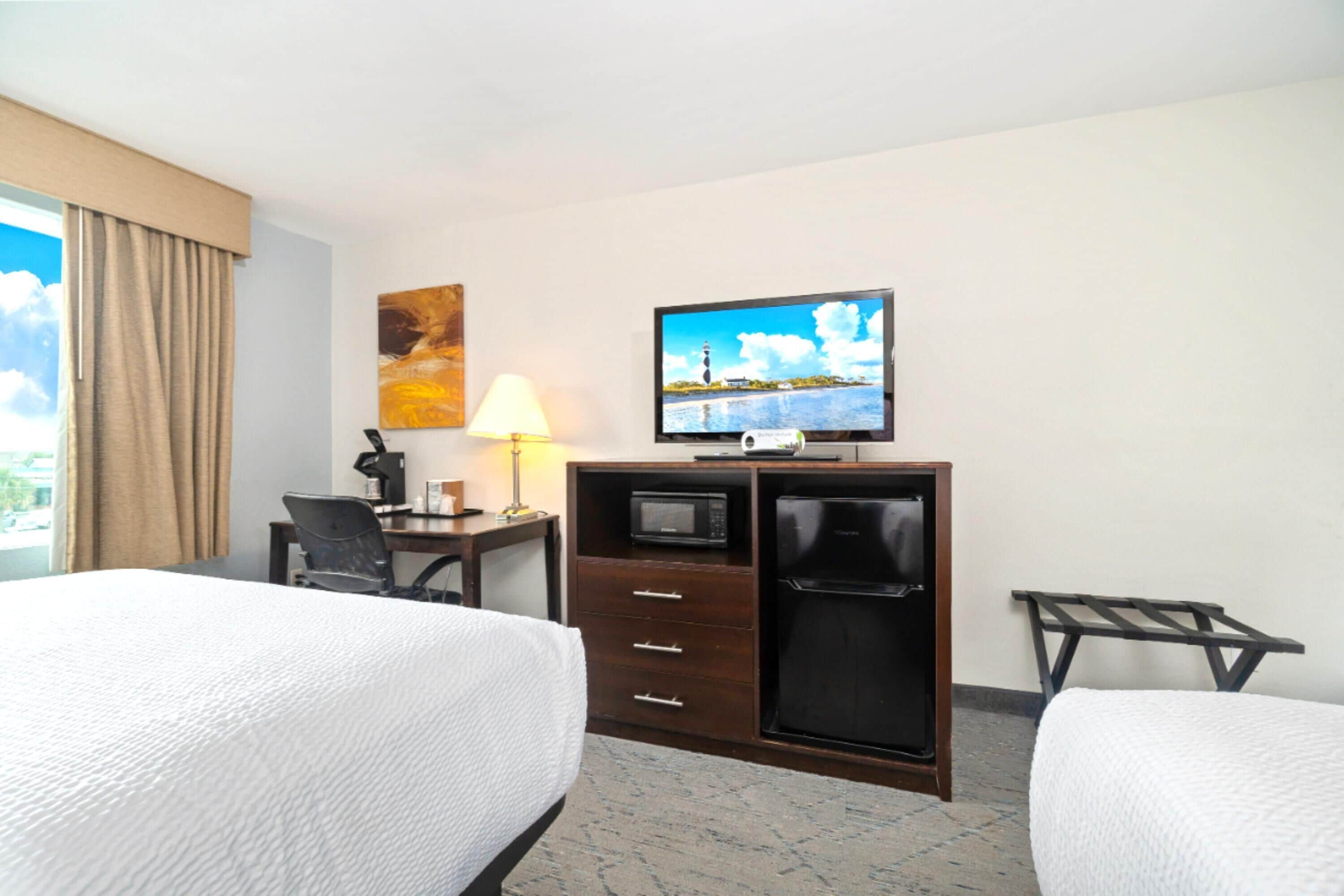 Une chambre d’hôtel avec deux lits, un bureau avec une lampe, une télévision, un four à micro-ondes et un réfrigérateur.