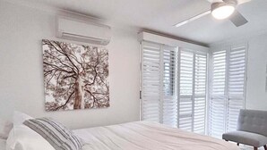 A bedroom with a bed, a ceiling fan, a window with blinds, and a wall-mounted air conditioner. - Premier Oceanfront - Large spacious 3 Bedroom in Resort (Point Lookout)