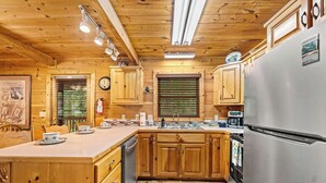 Une cuisine rustique, située dans une cabane en bois, avec un îlot central, des armoires en bois et un réfrigérateur en acier inoxydable.