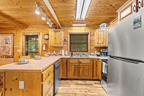 A wooden cabin kitchen with a central island, wooden cabinets, and a stainless steel refrigerator. - NEW! Wandering Bear-PRIVATE 3BR/3BA Cabin w/ HT & FP (Sevierville)