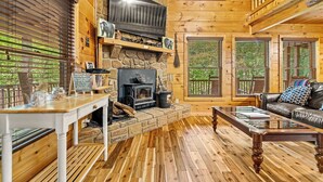 Un intérieur de chalet chaleureux avec une cheminée en pierre, des murs en bois, un téléviseur et un coin salon confortable.