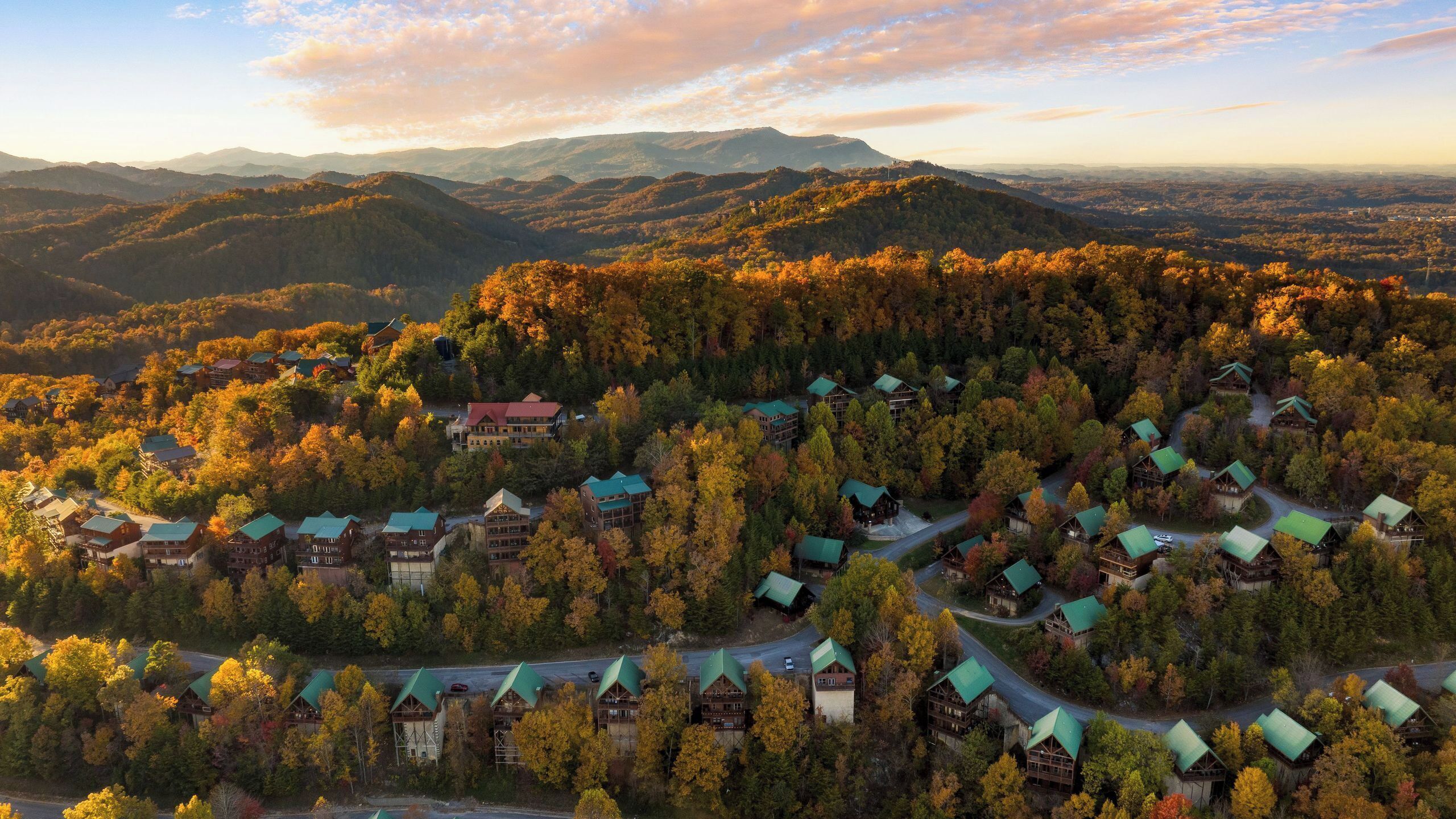 Een resort met meerdere bungalows, omringd door beboste heuvels en bergen.