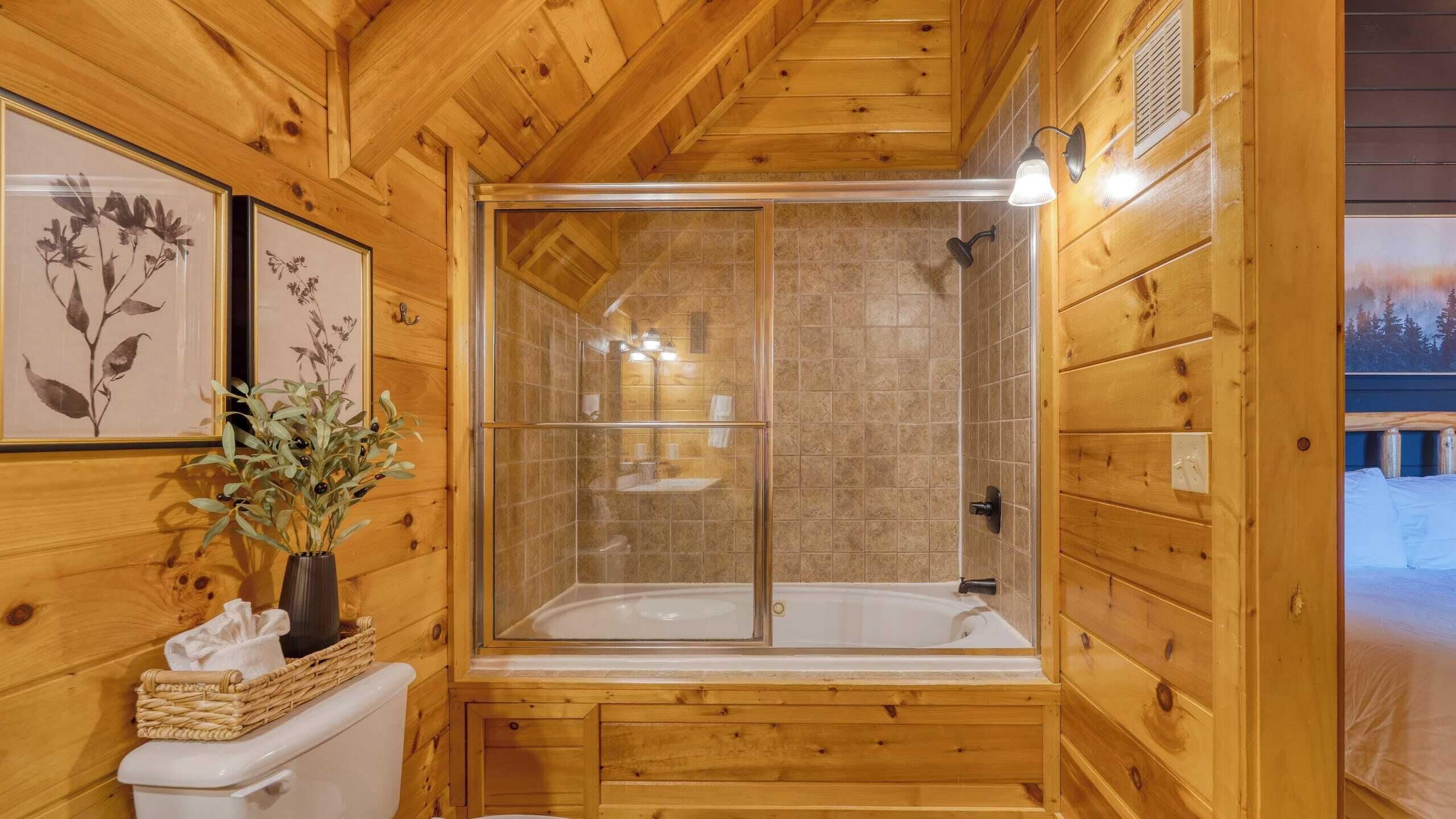 A wooden cabin bathroom with a glass-enclosed shower, a white toilet, and a sink.